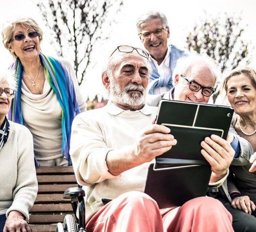 Elderly people around a bench watching a tablet